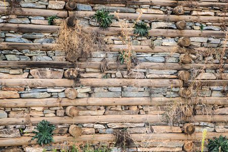 Weathered timber beams and stacked stones form a textured rural retaining wall with natural vegetation between the layersの写真素材