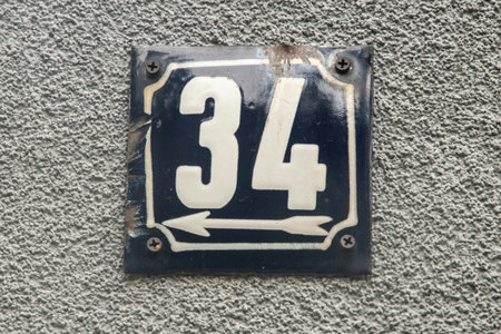 Old weathered vintage metal house number plate 34 mounted on textured urban wall