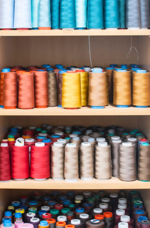Shelves with colorful sewing thread cones in professional tailoring atelier, textile production and...