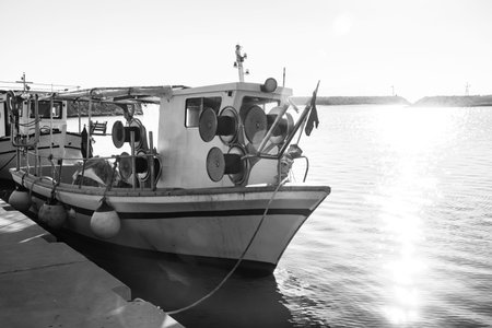 Small vintage fishing boat moored in calm Mediterranean harbor at sunset representing traditional coastal livelihood and maritime culture.の写真素材