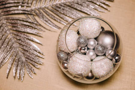 Christmas balls in glass with silver branch behind on creamy backdropの写真素材