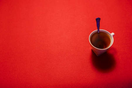A cup of hot tea with spoon on red backdrop