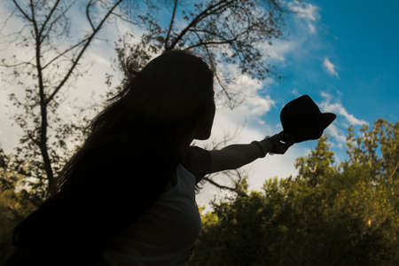 Low angle shot of young girl in silhouette raising her straw hat.Nice blue sky with cloudsの写真素材