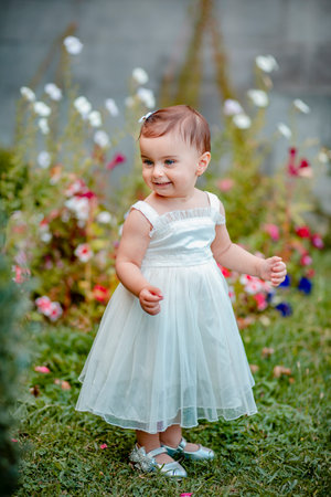 Cheerful baby girl with long white dress standing on grass in garden and smilingの写真素材