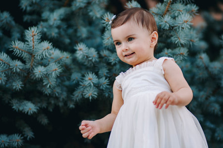 Nice baby girl with white dress standing in front of pine treeの写真素材