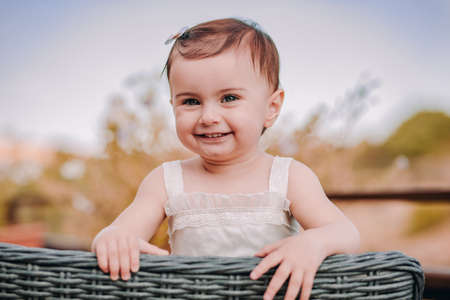 Happy baby girl sitting on straw chair looking at camera and smilingの写真素材