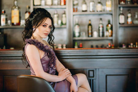 Luxury girl sitting and posing for camera in pub in front of bar with tasty cocktailsの写真素材