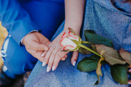 Engagement day. Just engaged young couple with blue dress holding hands with roseの写真素材