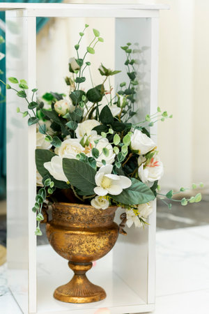 Closeup of wedding ornament. Artificial white flowers in metal vase on the floor in banquet hallの写真素材