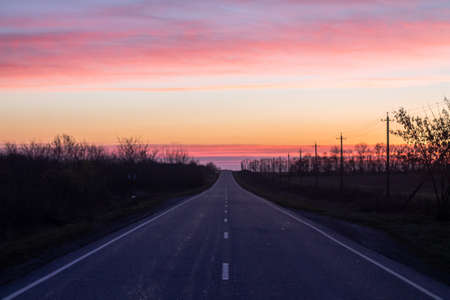 Asphalt road through the fields at sunset. Landscape with asphalt road at sunset