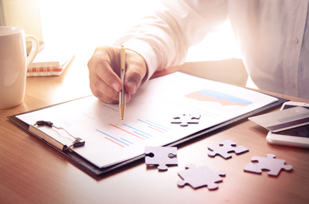 Businessman work with financial report at wooden office desk with puzzle pieces, smartphone, credit card and coffee cup. Concept for business, finance, marketing.の写真素材