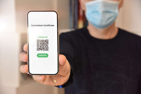 Digital certificate of vaccination against Covid-19. Man with face mask holding mobile phone with...