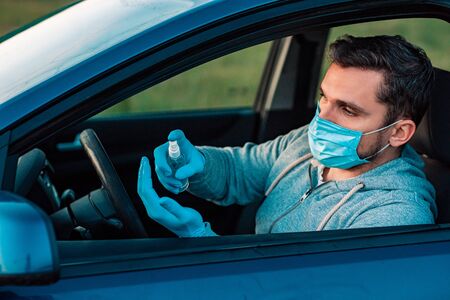 Young man using hand sanitizer or alcohol gel for washing hands in the car. Driver in a protective...
