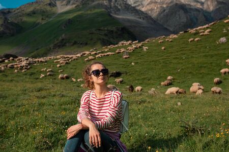 Beautiful young woman sitting with flock of sheepin on field background, nature.Young woman...
