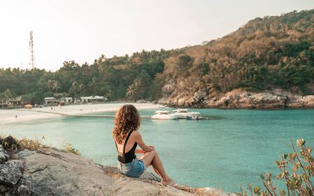 Happy woman sitting at the beach on a sunny day. Sexy perfect fit body woman. Portrait of glamour lady enjoying her vacation on beach shore. Back viewの写真素材