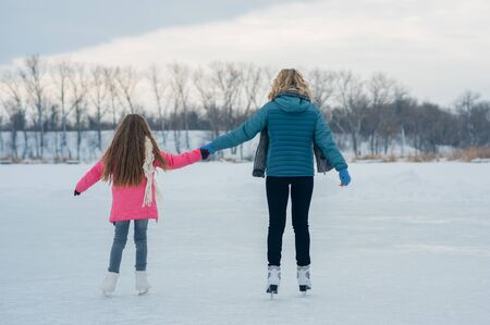 young mother and her cute daughter skates mittens tying shoelaces. They are prepare going to go...