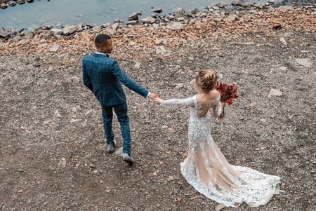 African groom and Caucasian bride embracing each other in a boho style with fresh flowers. Bride and...