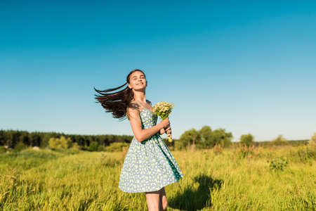 Beautiful teenage girl in blue dress standing back to camera on the summer field, Sun Light. freedom conceptの写真素材