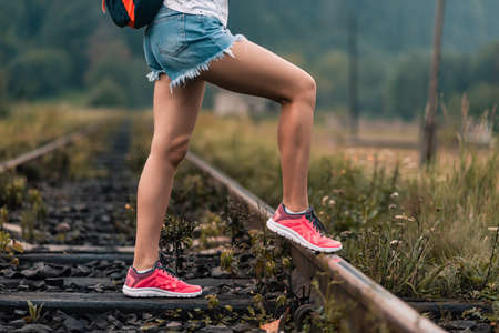 Girl in jeans shorts doing exercise, and demonstrates muscles standing on the railway tracksの写真素材