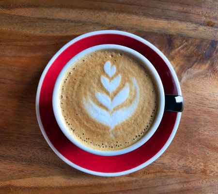 Flat white. Top view of hot coffee (cappuccino or latte) in red cup over brown wooden rustic background.の写真素材