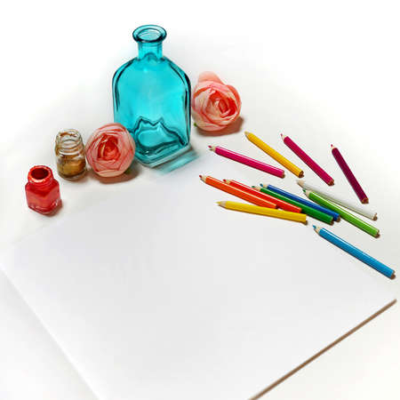 Flat lay scene in white tones for self employed freelance girl. Feminine little things as rose flowers, blue bottle, colored pencils and paper. Sketch Pad or notebook mockup.の写真素材