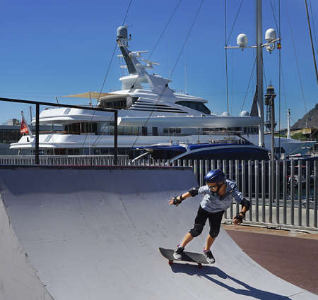 Teenage Caucasian boy skateboarding in skatepark near the pier. Active and healthy lifestyle concept. Summer sport activities.の写真素材