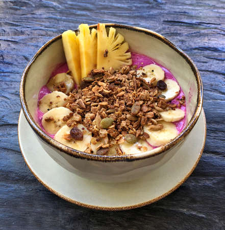 Pitaya breakfast bowl. White rustic black wooden background. Acai superfood smoothie bowl with pineapple slices, banana, dragon fruit smoothie, granola. Overhead, top view, flat lay, copy space.の写真素材