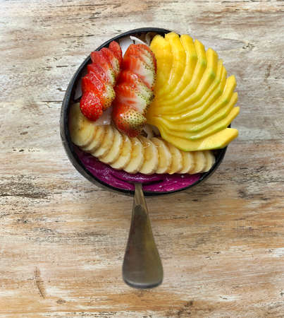 Pitaya breakfast bowl. Acai superfood smoothie bowl with mango, strawberry, banana, dragon fruit, granola and coconut flakes. White rustic wooden background. Overhead, top view, flat lay, copy space.の写真素材