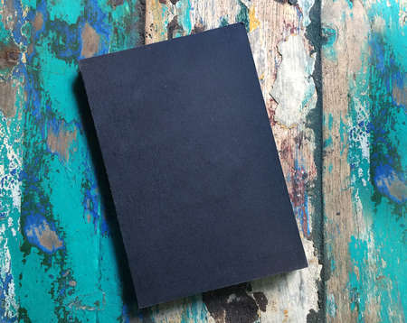 Black blank notebook or book cover on rustic painted wooden background. Lettering or art flat lay mockup. Shabby chic style. Vintage rustic composition. Copy space for text or design. Top view.の写真素材
