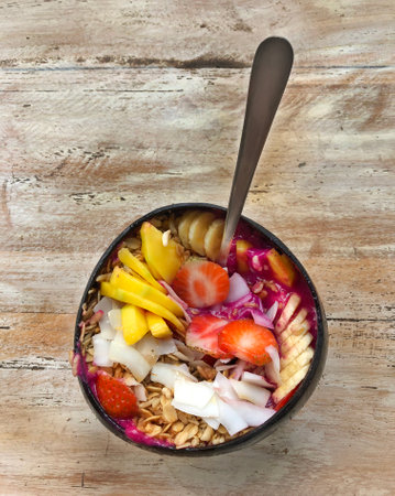 Pitaya breakfast bowl. Acai superfood smoothie bowl with mango, strawberry, banana, dragon fruit, granola and coconut flakes. White rustic wooden background. Overhead, top view, flat lay, copy space.の写真素材