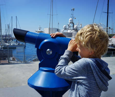 Teenage Caucasian boy looking through coin operating panorama telescope to the city seascape. Blue binoculars for travelers.の写真素材