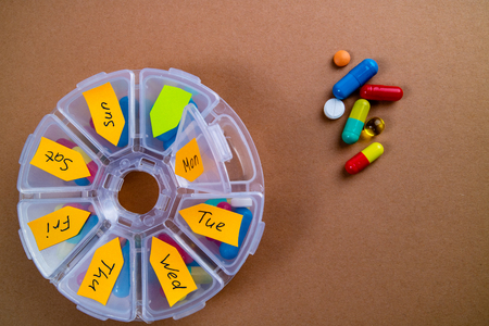 Weekly organizer with pills on brown background. Pharmaceutical medicine tablets, capsules and pills in round boxの写真素材