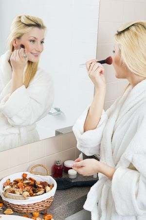 A young woman applies makeup in front of a bathroom mirror. Vertical shot.の写真素材