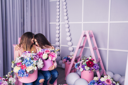 Two beautiful girls in jeans and pink sweater in studio with decor of flowers in basketsの写真素材