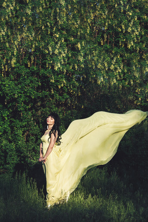beautiful girl in yellow dress in park on background of flowering shrubs.の写真素材