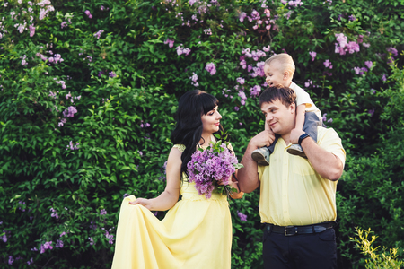 Happy family in park with blooming lilac. Mom, dad and son happy walk at sunset. Concept of happy family. Son sits on shoulders of pope.の写真素材