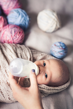 baby lies on bed among tangles of threads and drinks milk from bottle.の写真素材