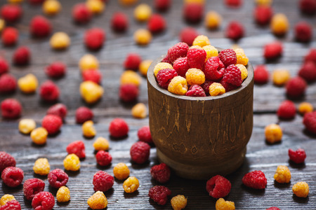 Organic yellow and red raspberries in wooden pot on wooden background
