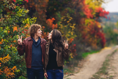 cheerful couple shows emotions. man and woman in leather jackets and jeans show each other tongues against background of autumn treesの写真素材