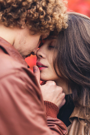 Curly-haired mustachioed man and brown-haired woman hugging in autumn against background of red trees. Happy couple in loveの写真素材