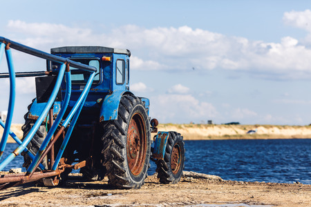 old tractor with trailer stands on shore of sea bayの写真素材