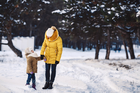 Beautiful young mother and her little daughter are walking holding hands in the winter forestの写真素材