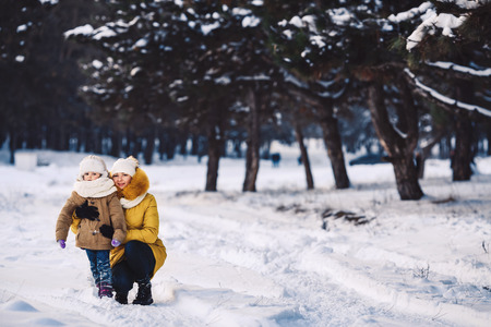 Beautiful young mother and her little daughter are hugging in the winter forestの写真素材