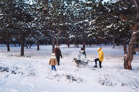 Happy young caucasian family plays with a dog in winter in a pine forest. Photo for advertising...