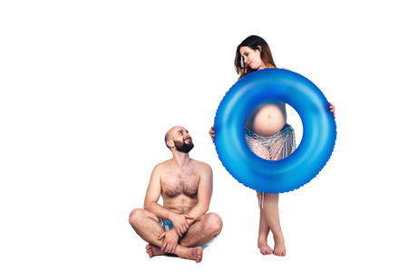 happy pregnant couple on summer sea vacation. a pregnant girl and a bearded man with an inflatable circle. isolated on whiteの写真素材