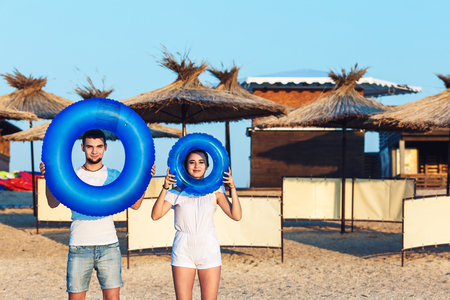 man and woman are posing on the beach and holding inflatable circles. concept of summer sea holidayの写真素材