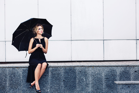 gorgeous woman with an umbrella sits on the parapet and waitsの写真素材