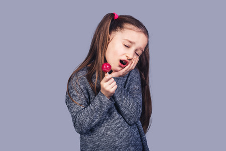 little sad girl with a red lollipop in her hands, whose teeth hurt. The concept of caries...