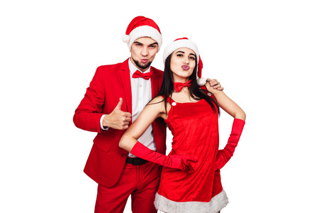 young couple having fun at a christmas theme party. young man and woman in red suits with Santa hats. isolated on whiteの写真素材