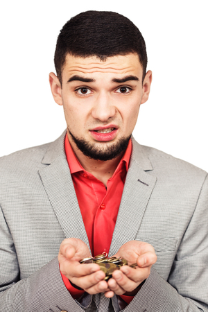 The guy is distressed by the lack of money. young sad bearded man holds coins in his hands. isolated on whiteの写真素材